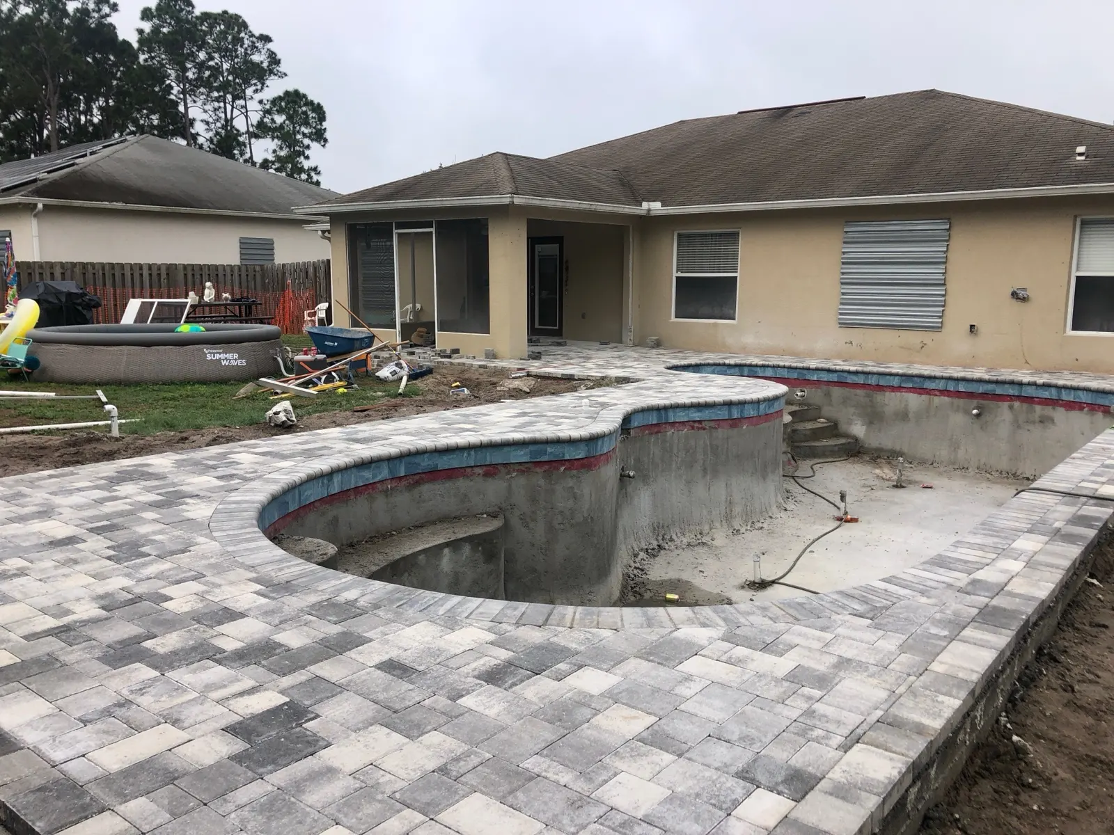 Paver coping course set on the exposed bond beam of a pool before the deck field goes in, Brevard County